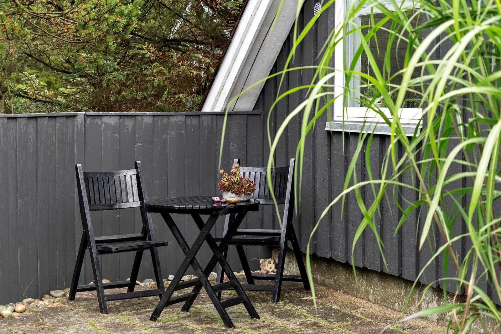 Outdoor area with table and two chairs in front of a gray house.