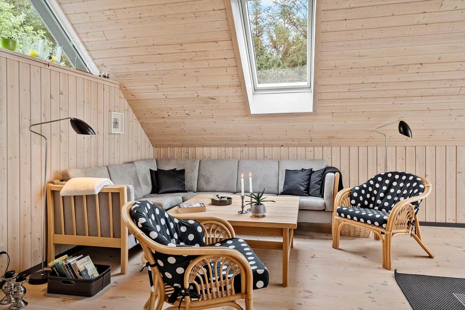 Living room with wood walls, sofa, two rattan chairs with polka-dot cushions, and table.