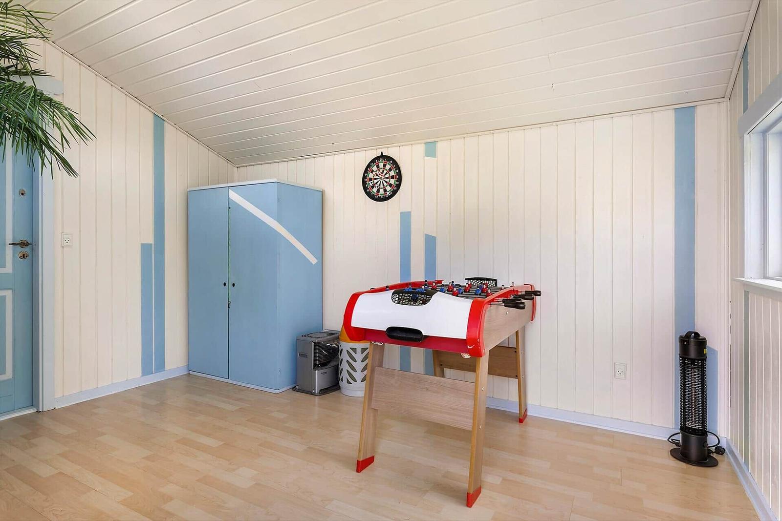 Room with foosball table, dartboard, and blue cabinet against wood wall.