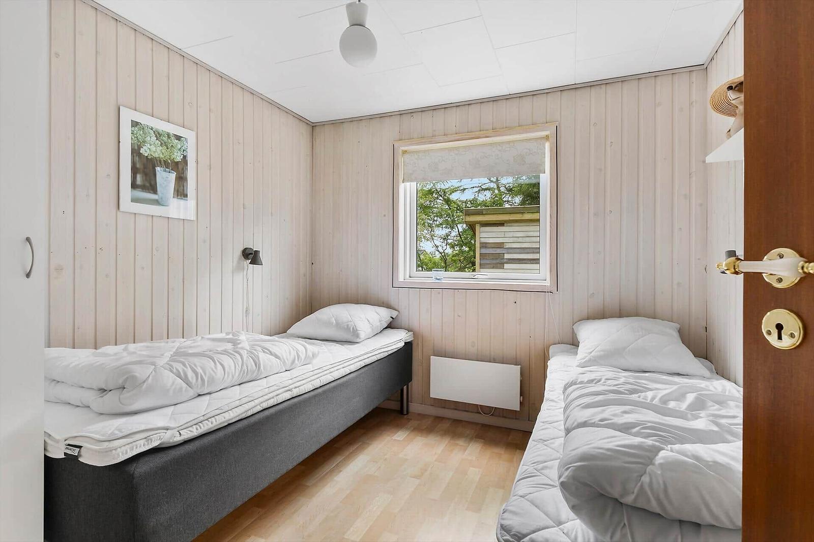 Two beds with white bedding, wood-paneled walls, and window with view of outside.