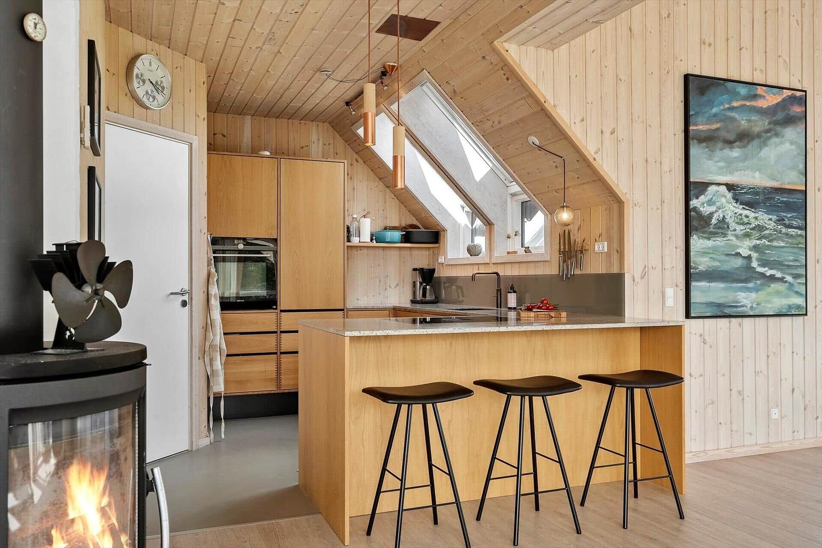 Küche mit Holzwand, Insel und Sitzhöhe. Dachfenster und Kamin sichtbar.