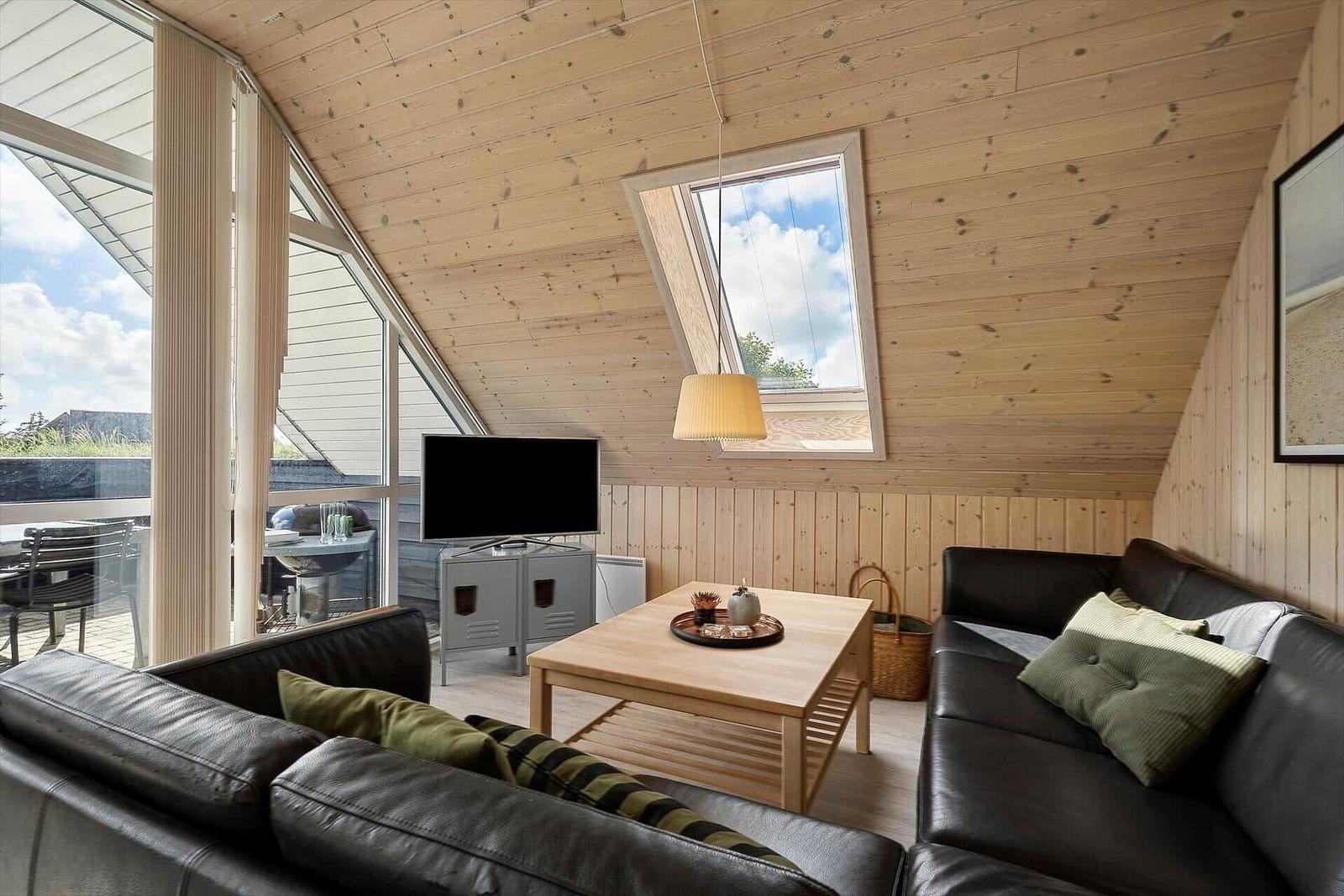 Wohnzimmer mit Holzwand, Sofa, TV und Sitzgelegenheit. Durchgang zur Terrasse.
