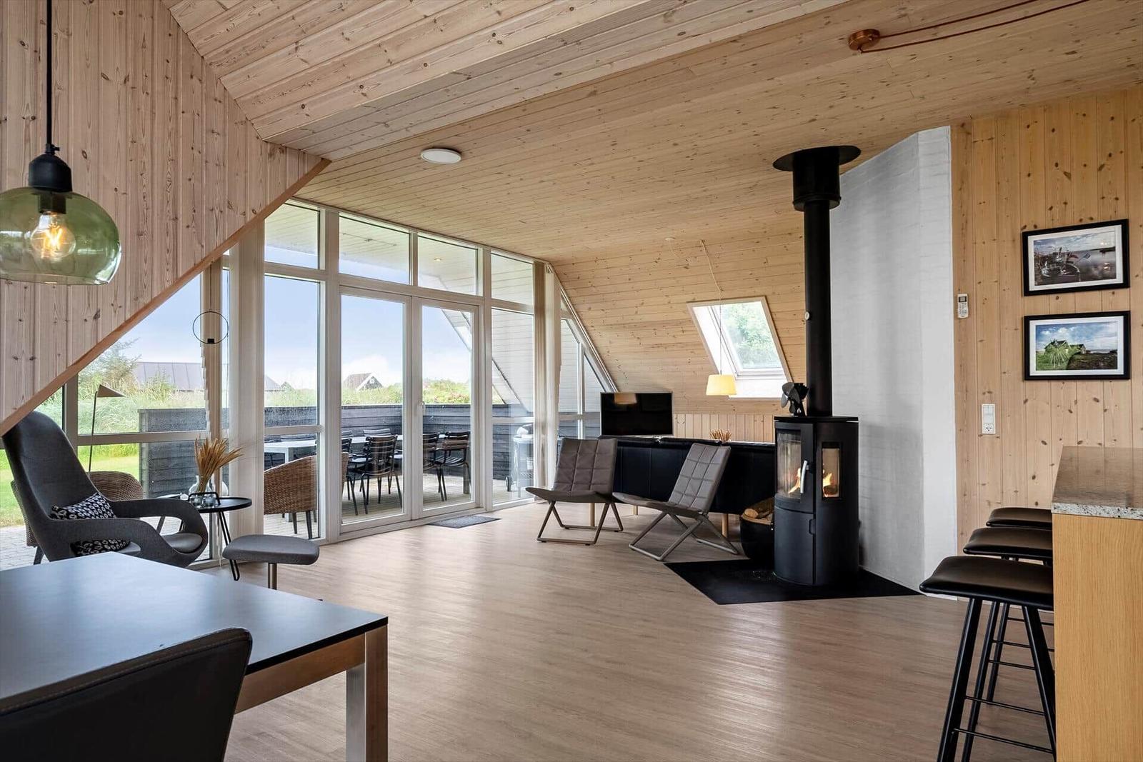 Wohnraum mit Holzdecke, Kamin und großem Fenster zur Terrasse.