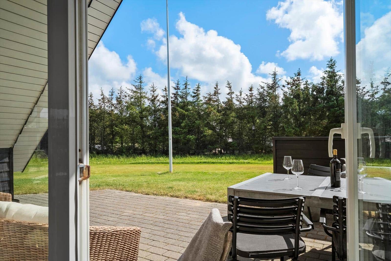 Terrasse mit Tisch, Stühlen und Weinglas unter blauem Himmel.