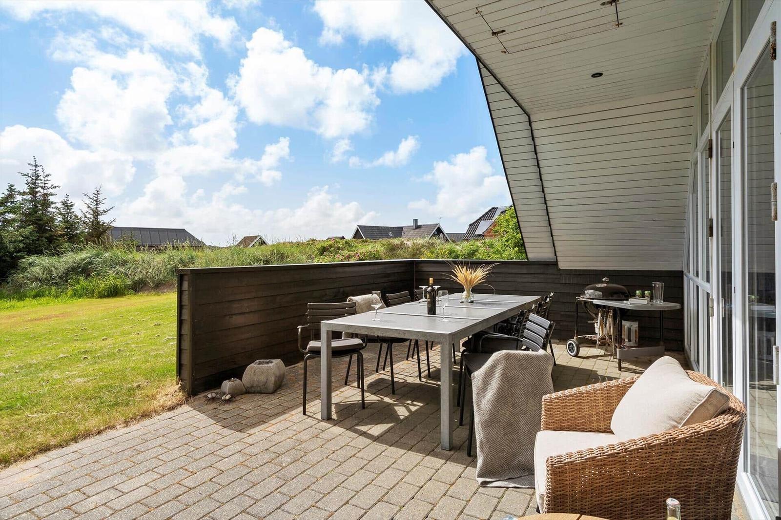Terrasse mit Tisch, Stühlen und Grill. Blick auf Grasland und Himmel.