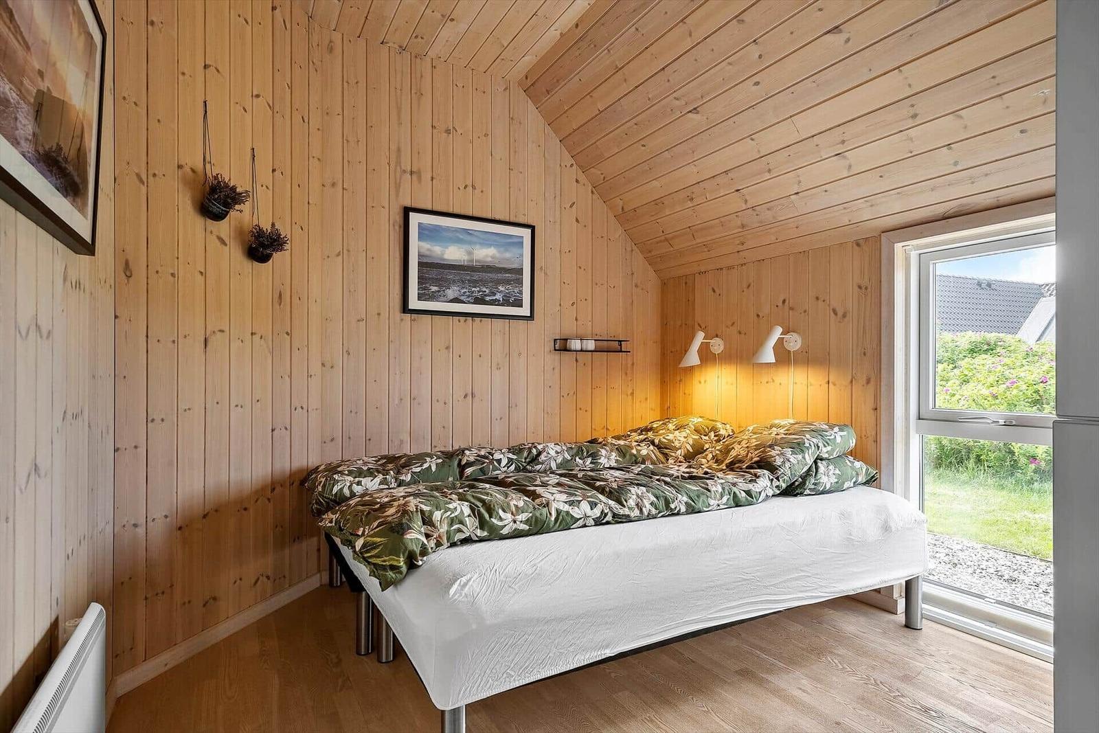 Schlafzimmer mit Holzwänden, Bett und Fenster zum Garten.