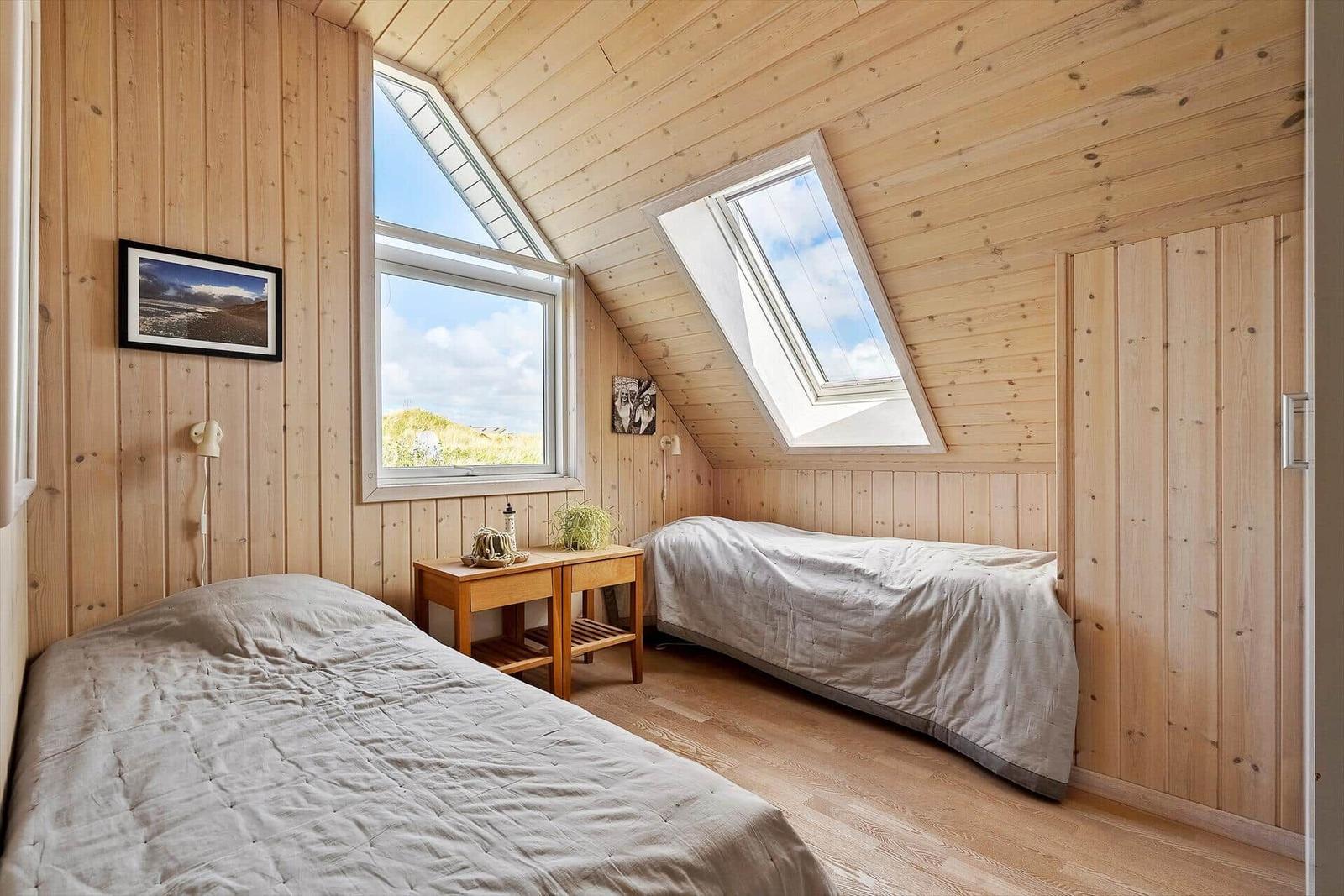 Zwei Betten in einem Holzhauszimmer mit Dachfenstern und Wandbildern.