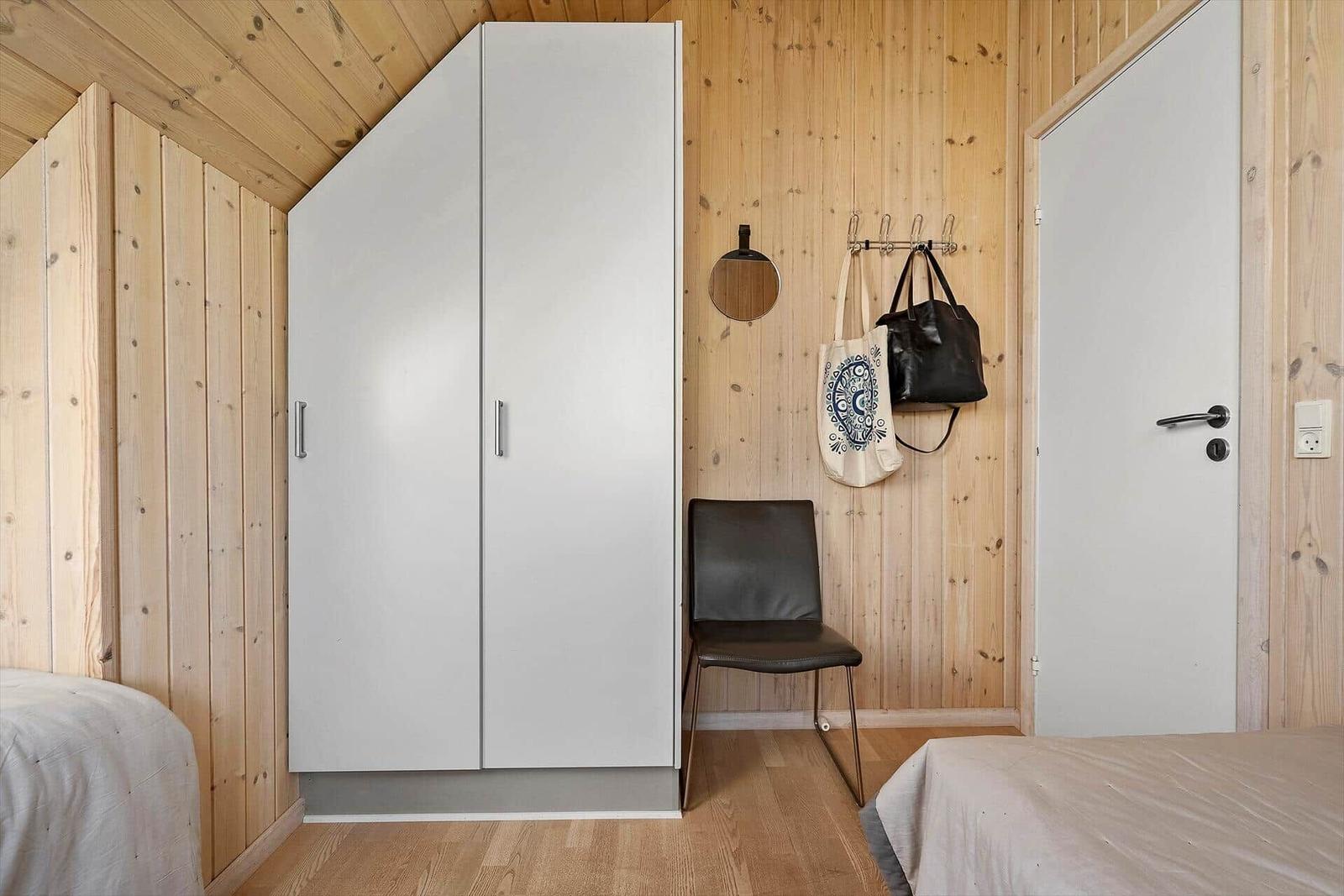 Schlafzimmer mit Holzwand, Kleiderschrank, Stuhl und Tür.