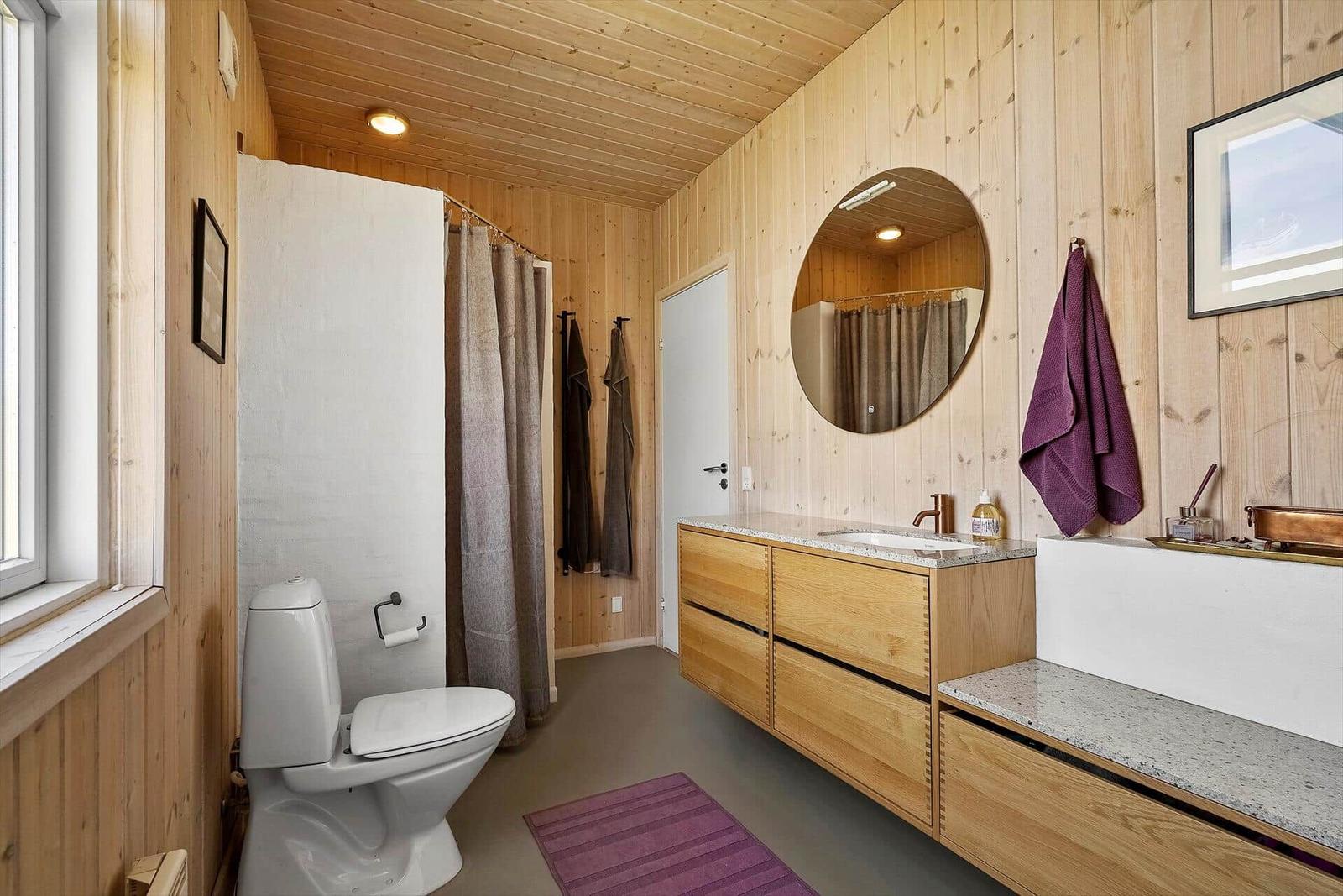 Badezimmer mit Holzwand, Waschbecken, Toilette und Dusche.