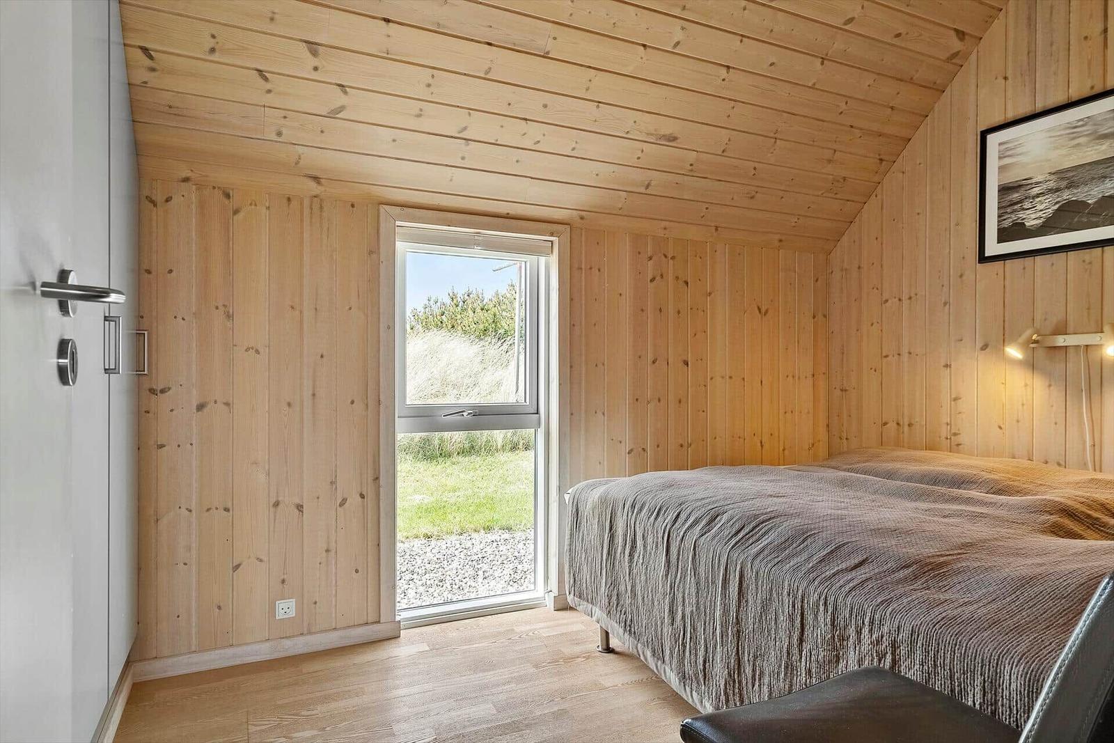 Schlafzimmer mit Holzwand, Bett und Fenster zur Außenseite.