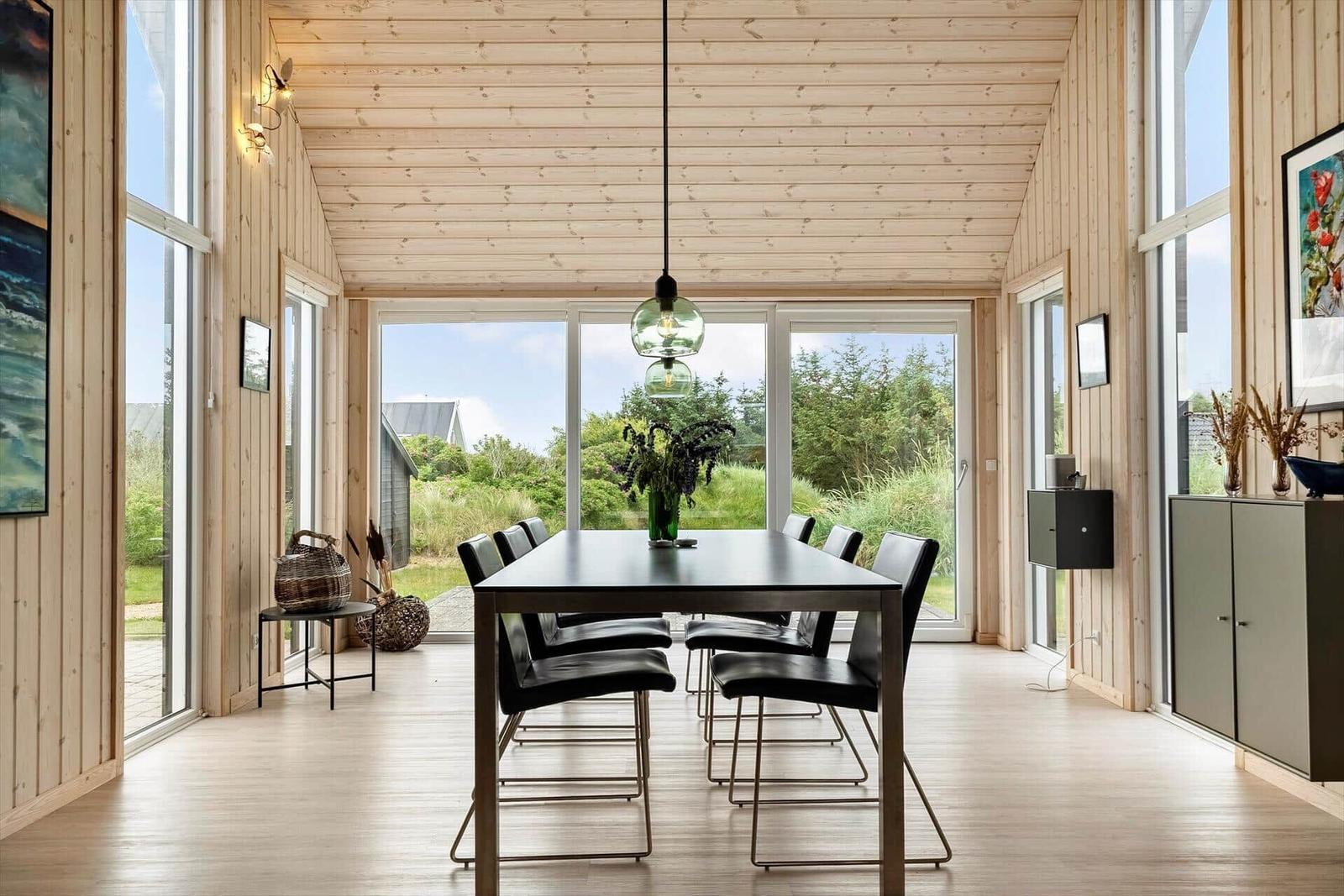 Essbereich mit Tisch und Stühlen, große Fenster, Holzwände und Decke.