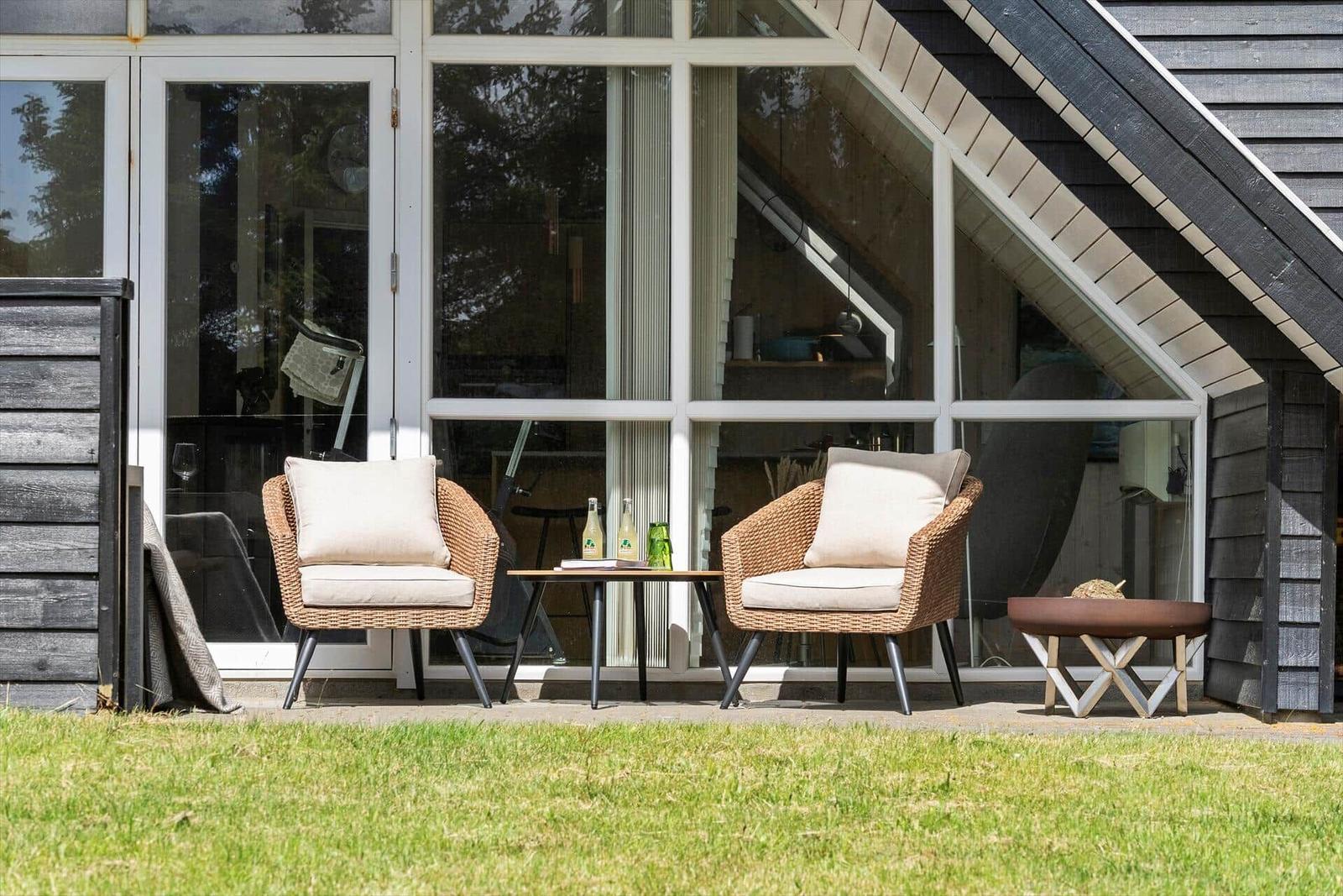 Außenbereich mit zwei Stühlen, Tisch und Sitzbank vor einem Haus mit großem Fenster.