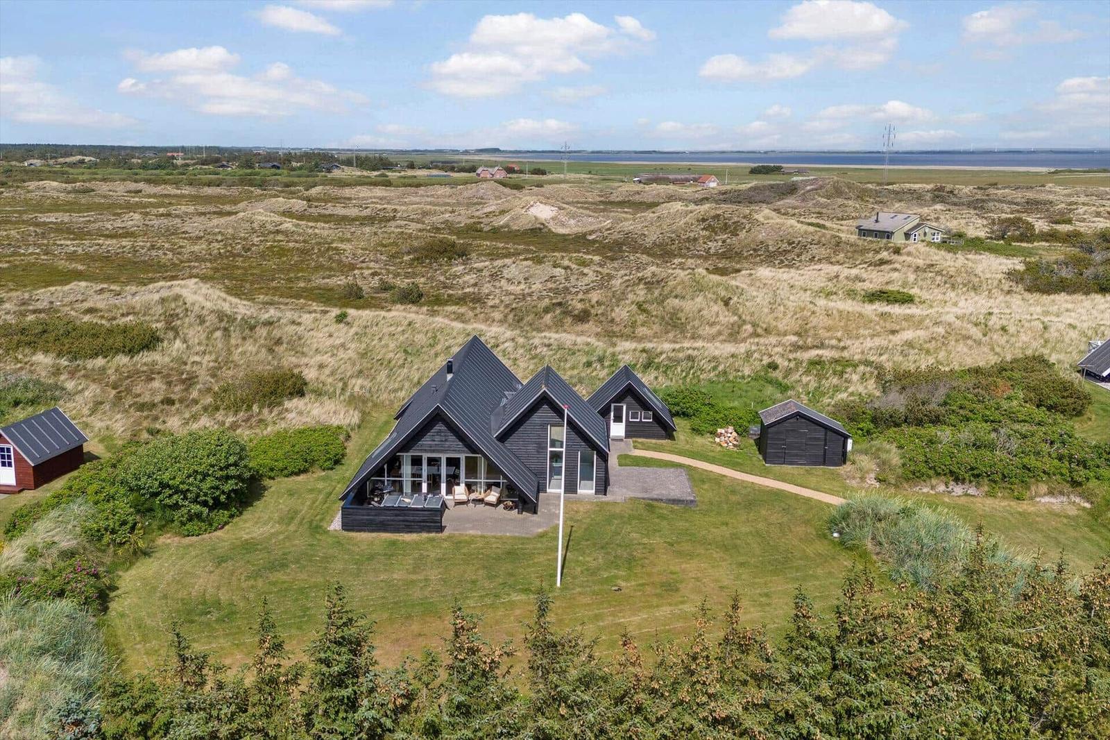 Schwarze Holzhütte mit großem Garten und Blick auf Dünenlandschaft.