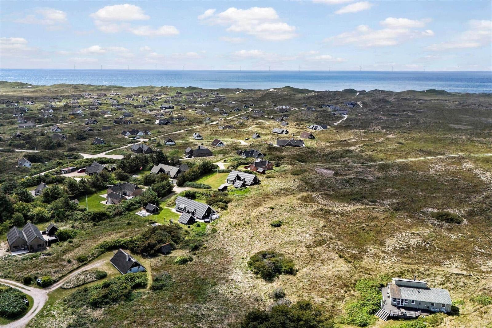 Aerial view of coastal holiday homes with wind turbines on the horizon.