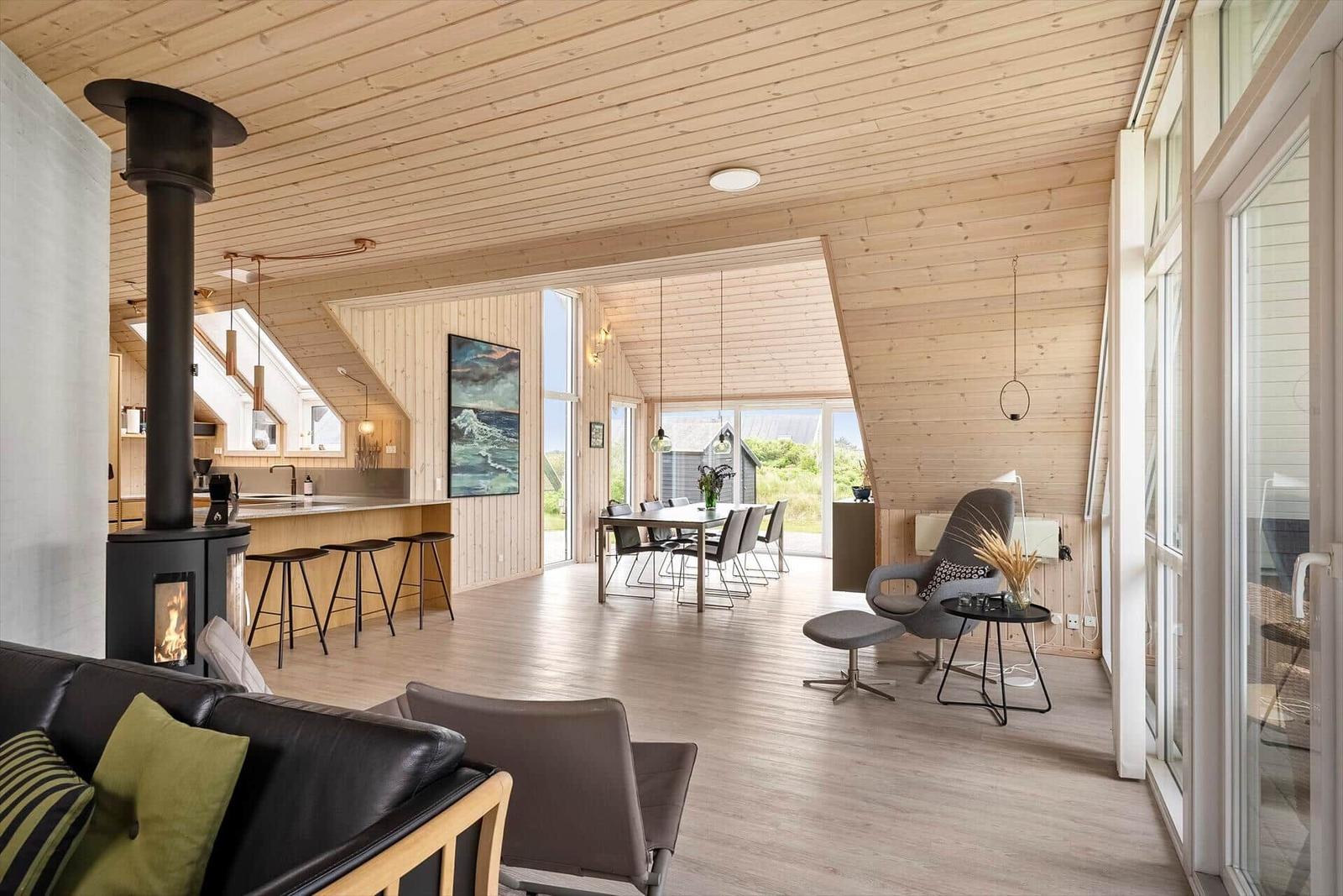 Großer Wohnraum mit Holzdecke, Kamin und Essbereich mit Blick nach draußen.