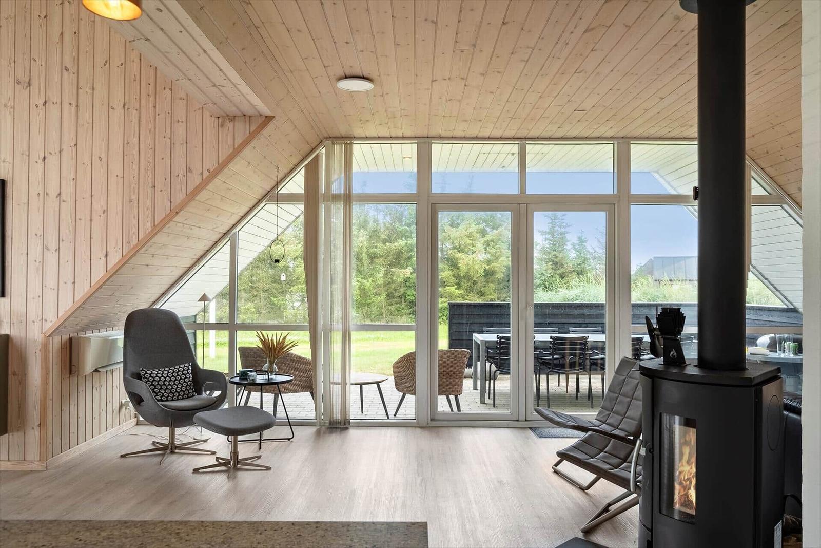 Wohnraum mit Holzwand, Kamin und großem Fenster zum Garten.