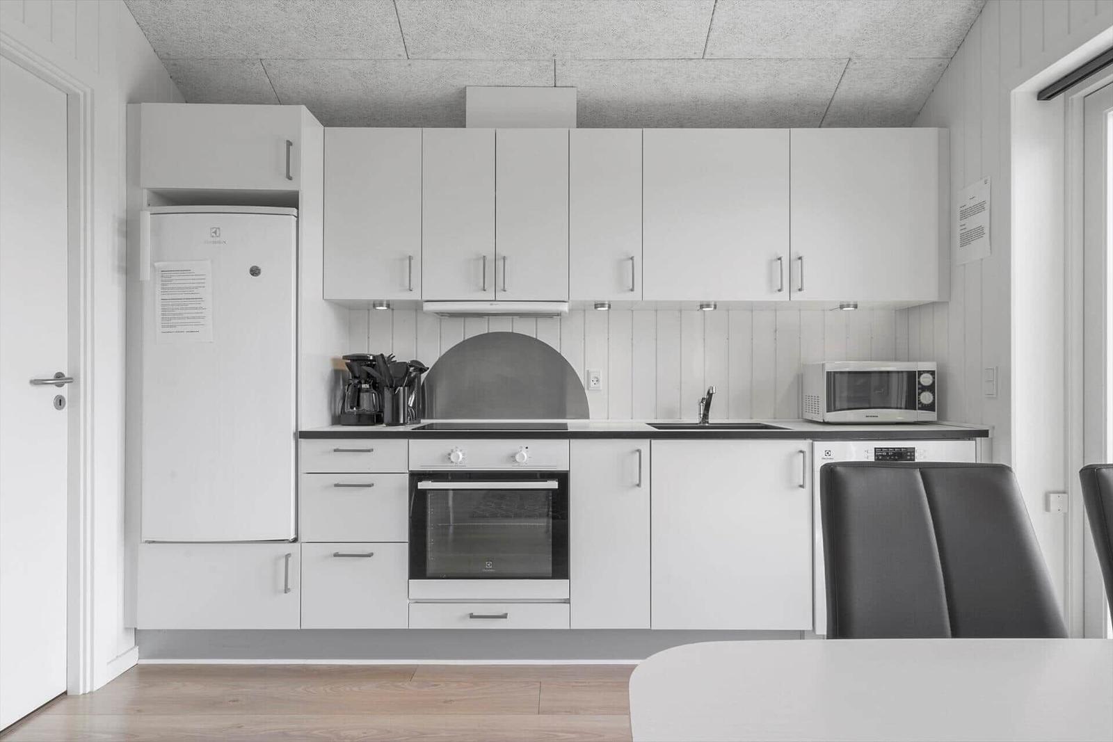 Küche mit weißen Schränken, Herd, Kühlschrank und Mikrowelle.