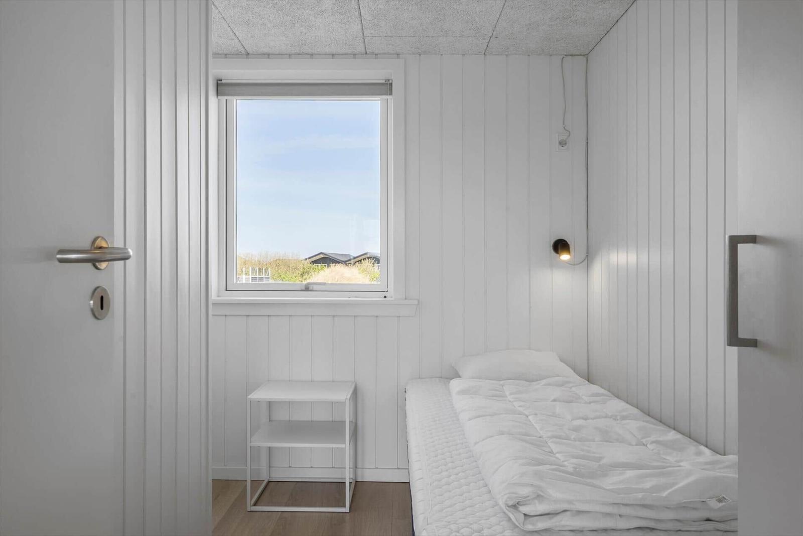 Ein Schlafzimmer mit weißem Bett, Fenster und Nachttisch.
