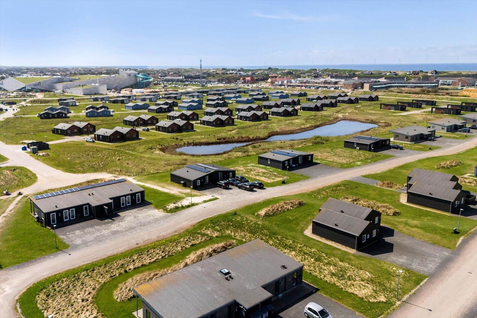 Aerial view of holiday homes with green fields and a small pond.