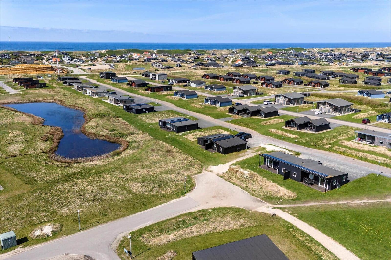 Aerial view of holiday homes near the sea with green fields and a pond.