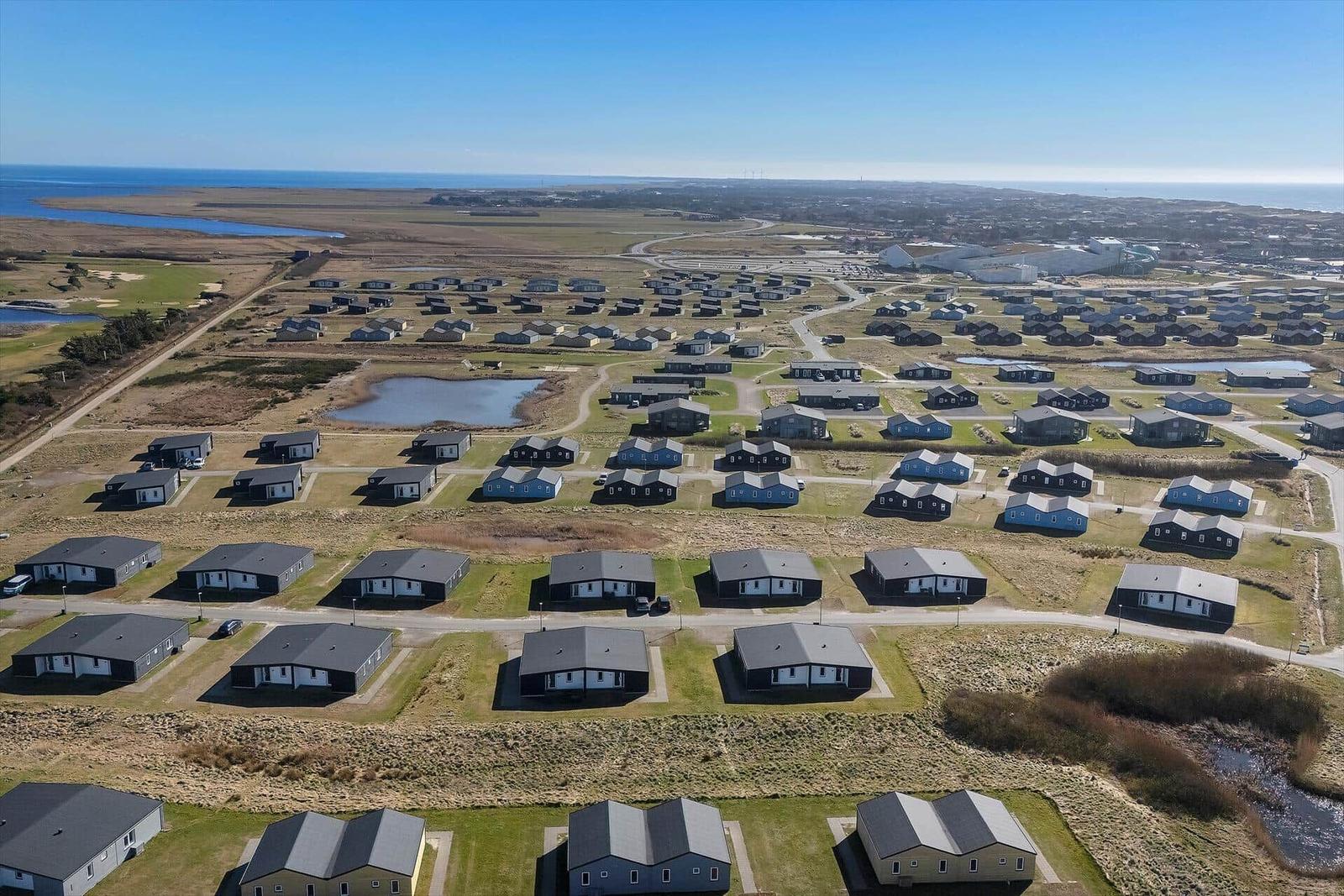 Aerial view of holiday homes near coastal area with ponds and open fields.