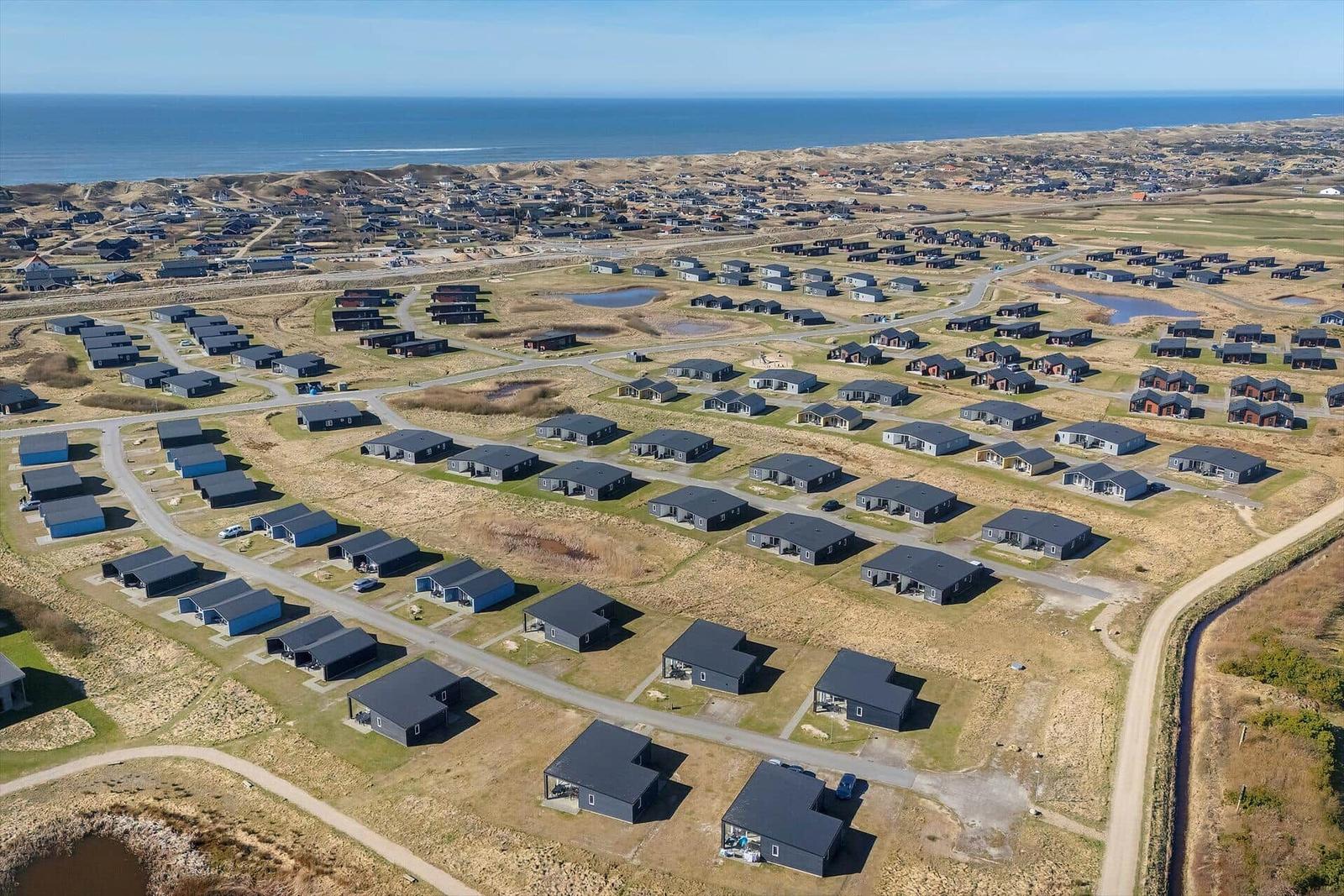 Aerial view of holiday homes near the sea with roads and small ponds.