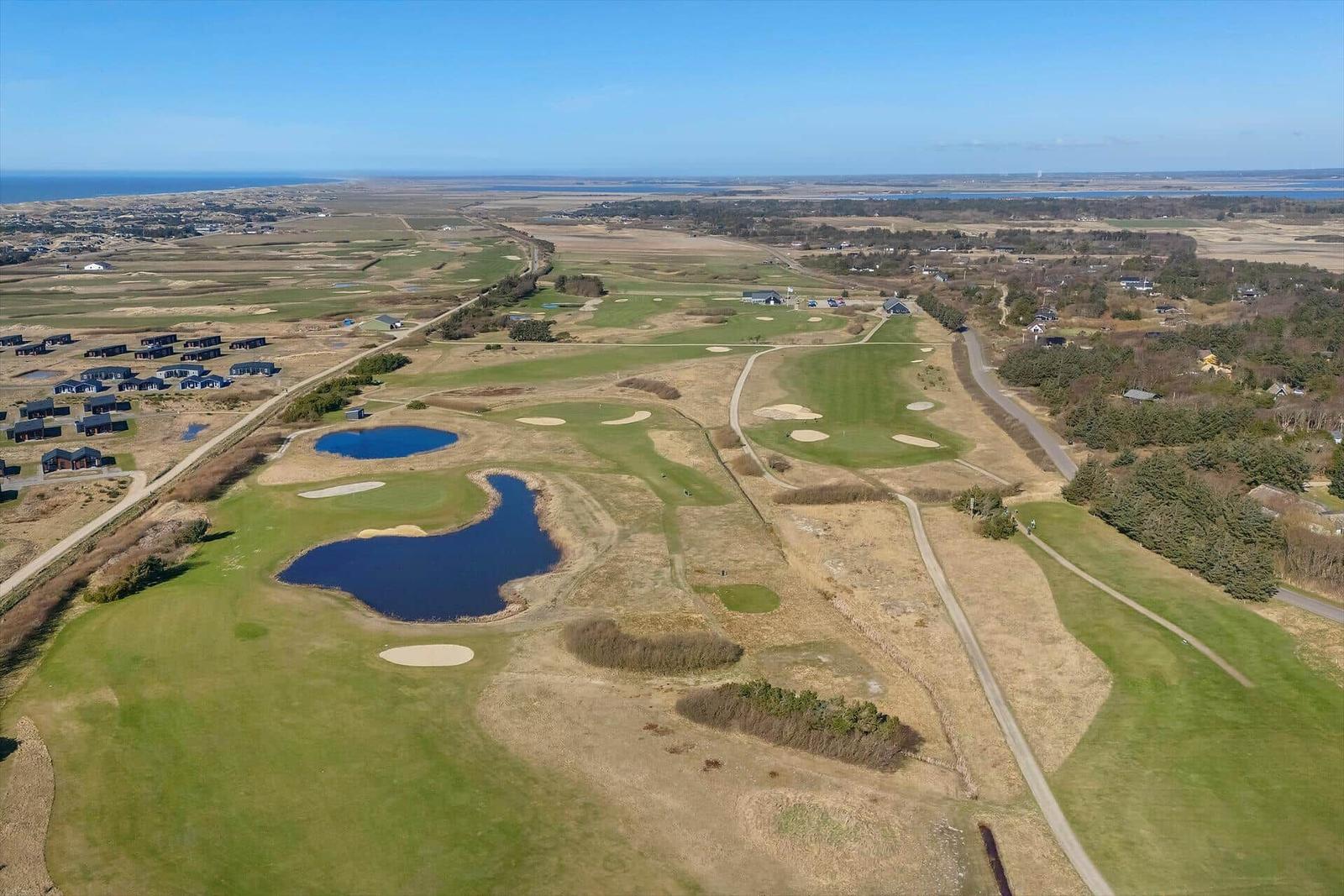 Luftbild eines Golfplatzes mit Seen und Sandbunkern, umgeben von Wiesen und Bäumen.