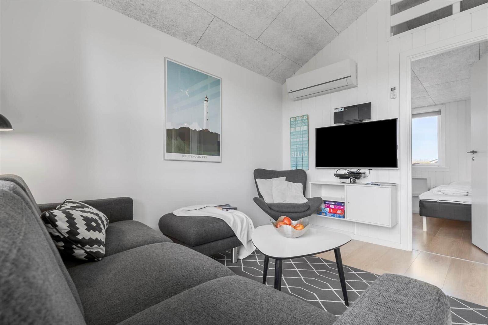 Wohnzimmer mit Sofa, Sessel und Fernseher. Blick in Schlafzimmer.