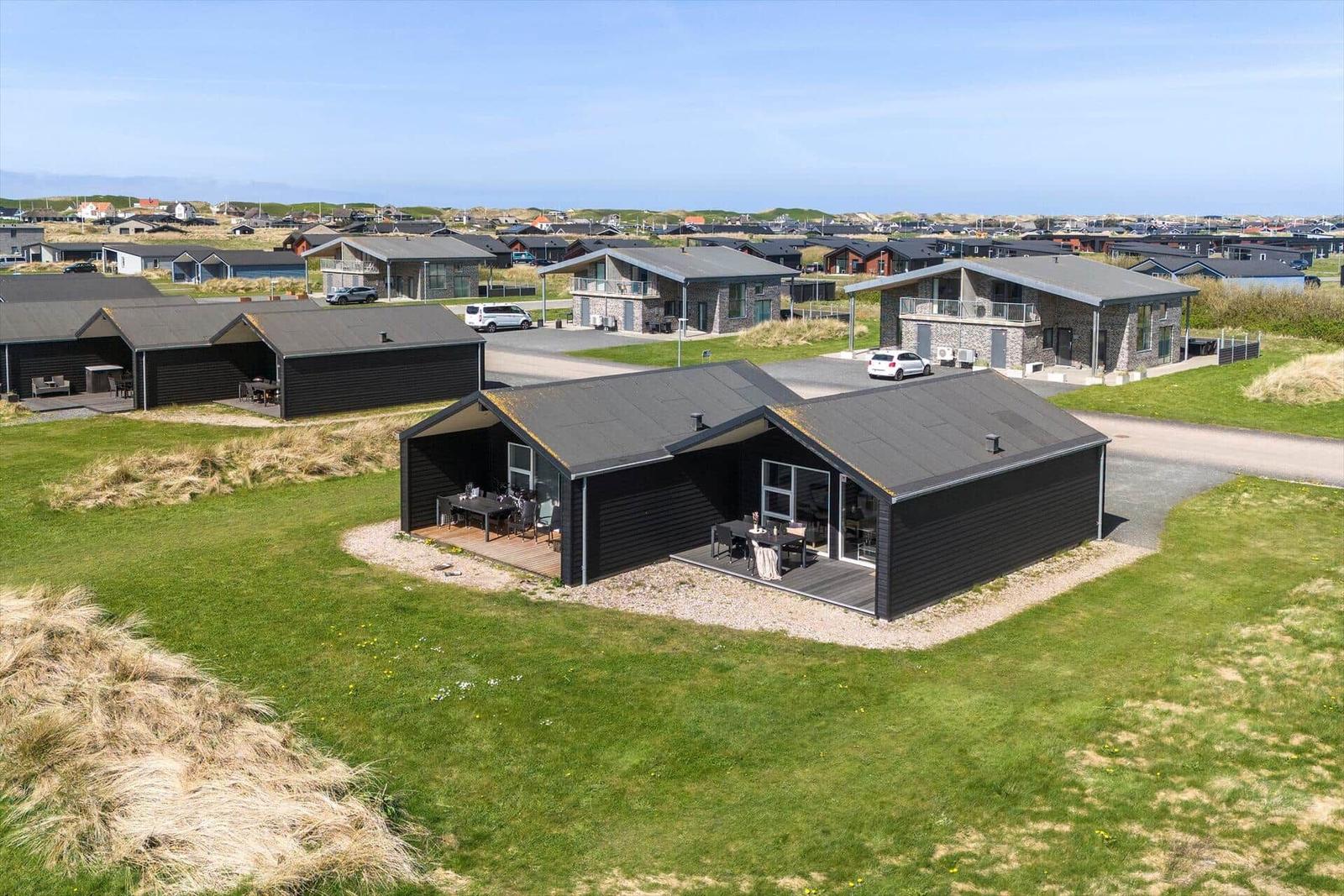 Modernes Ferienhaus mit Terrasse und Garten, umgeben von Gras und Dünen.