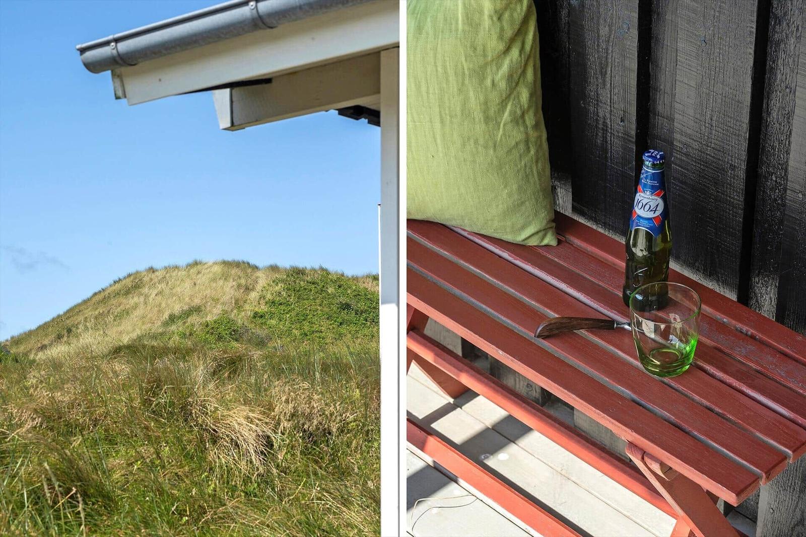 Terrasse mit Holzbank und grünem Kissen. Hintergrund: Grasbewachsener Hügel unter blauem Himmel.
