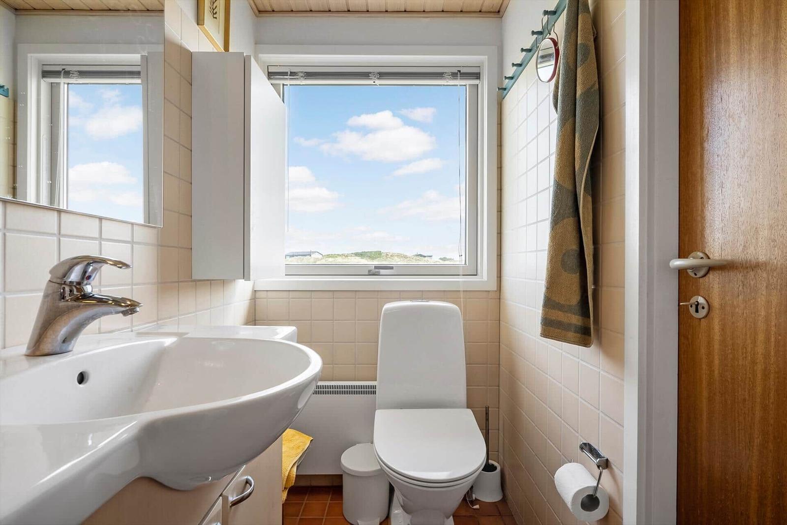 Badezimmer mit Waschbecken, Toilette und Fenster mit Blick auf die Landschaft.