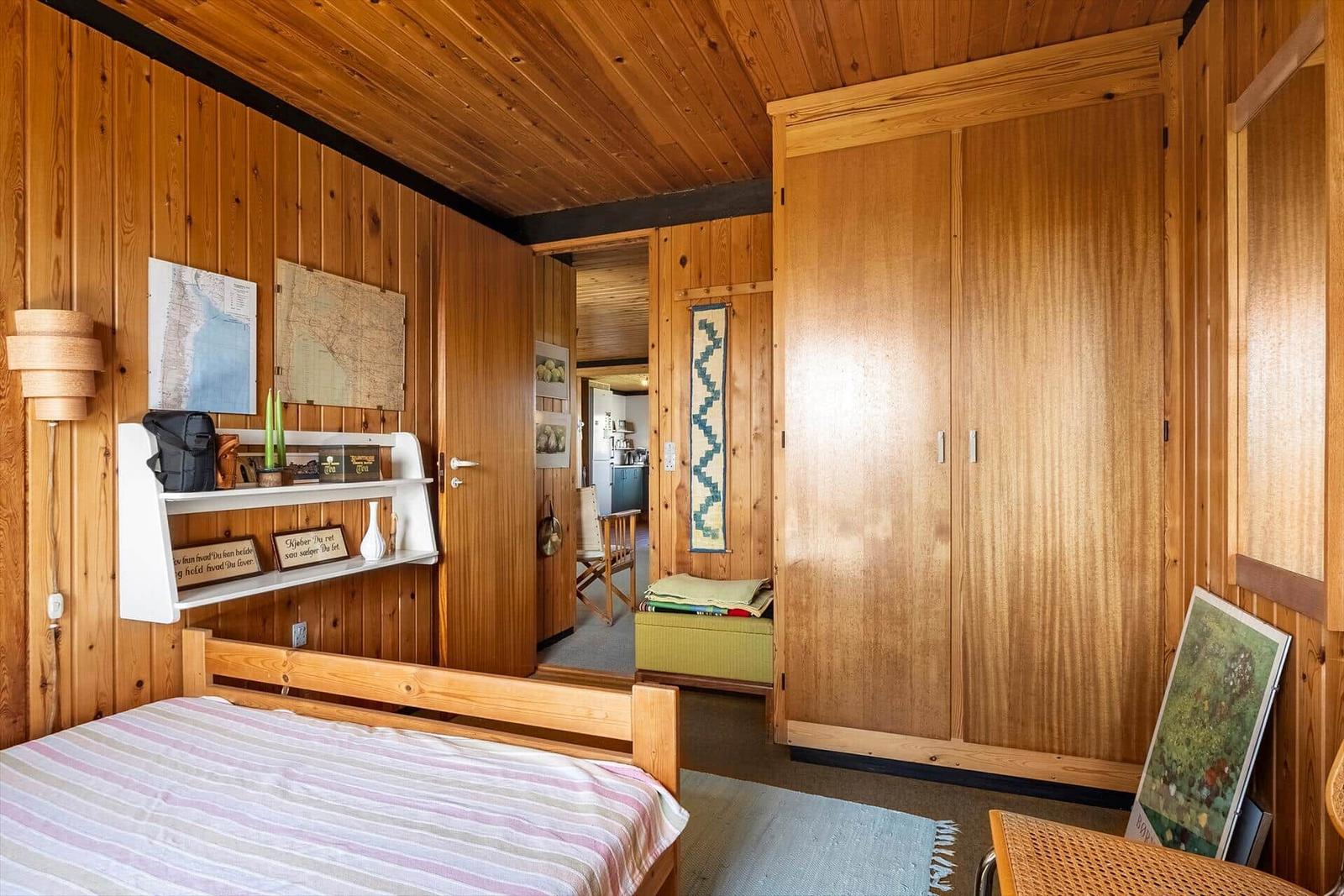Schlafzimmer mit Holzwand, Bett, Kleiderschrank und Regal mit Karten.