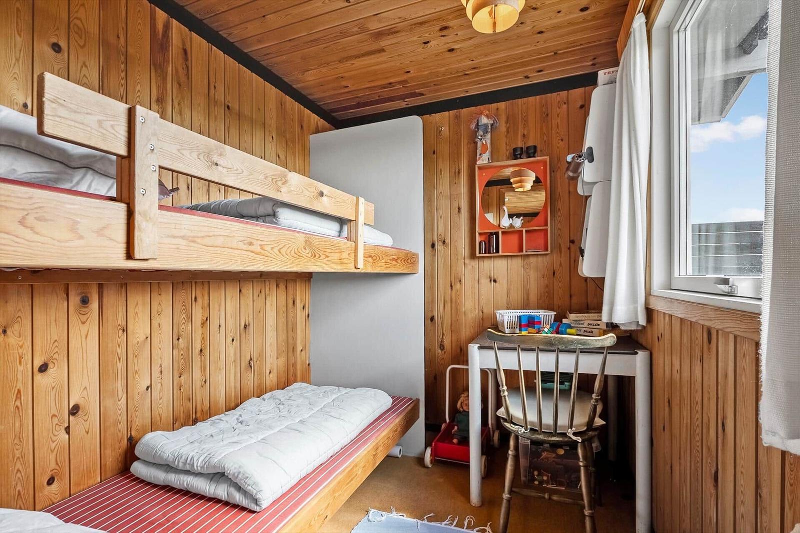 Zimmer mit Kojenbett, Schreibtisch und Fenster.