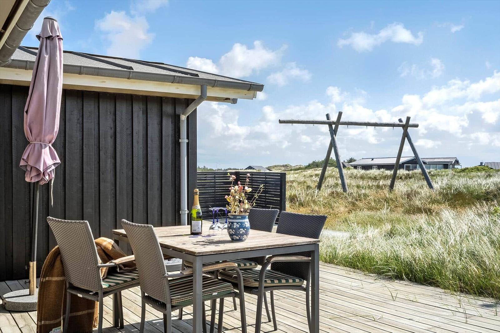 Terrasse mit Tisch, Stühlen und Sonnenschirm neben Holzhäusern.