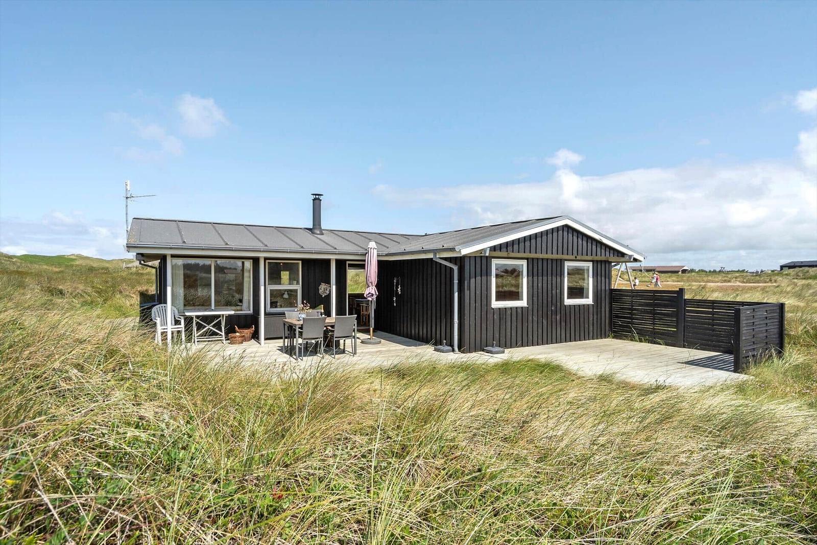 Moderne Holzhütte mit Terrasse und Garten. Außenbereich mit Tisch, Stühlen und Sonnenschirm.