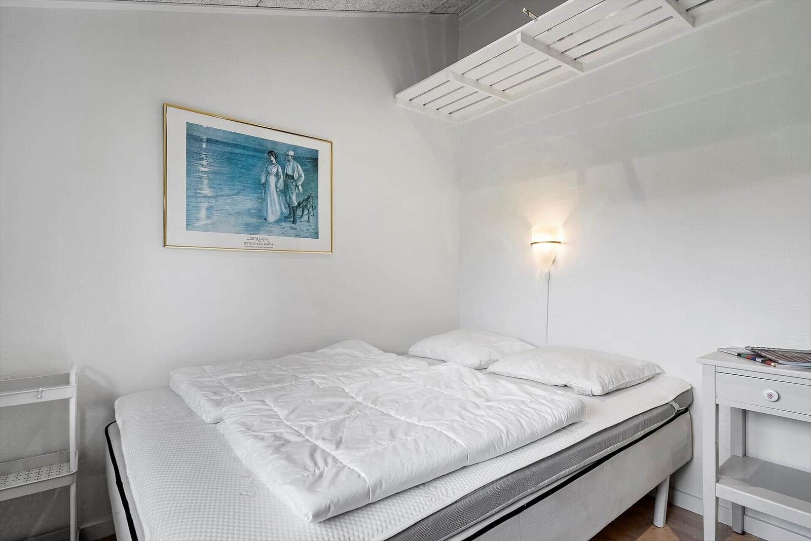 Schlafzimmer mit weißem Bett, Wandbild und Nachttisch.