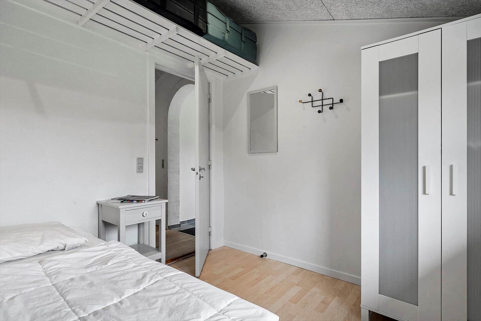 Schlafzimmer mit Bett, Kleiderschrank und Nachttisch. Hängende Koffer unter der Decke.