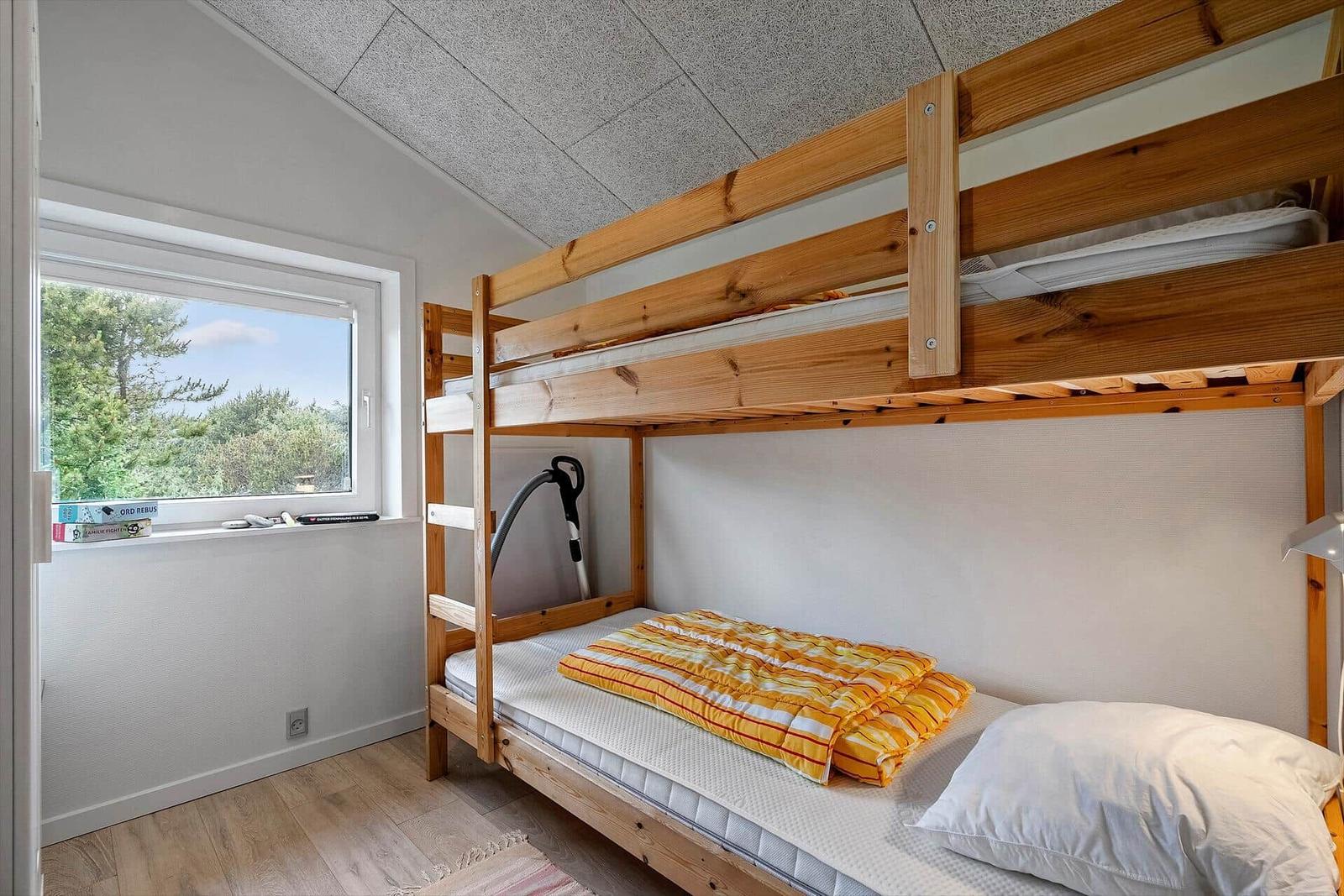 Ein Schlafzimmer mit Holzbett, Fenster und Blick auf Bäume.