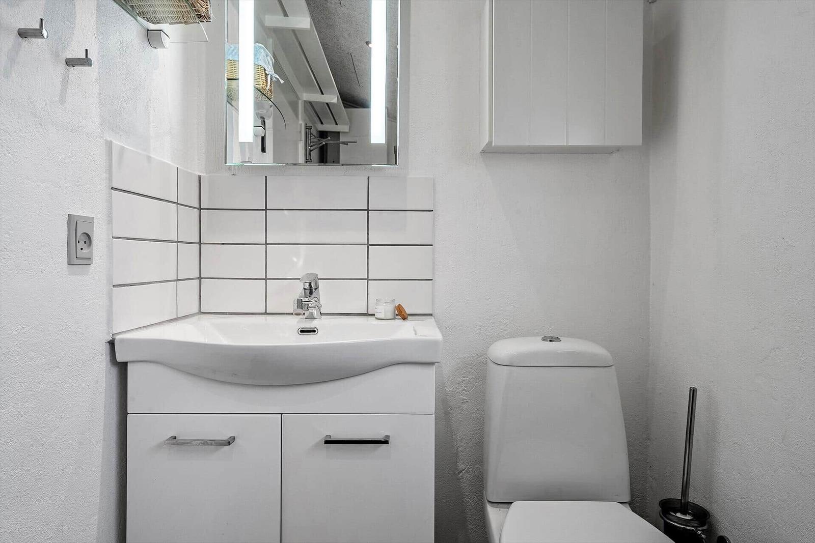 Badezimmer mit Waschbecken, Spiegel und Toilette. Weiße Fliesen und Wand.