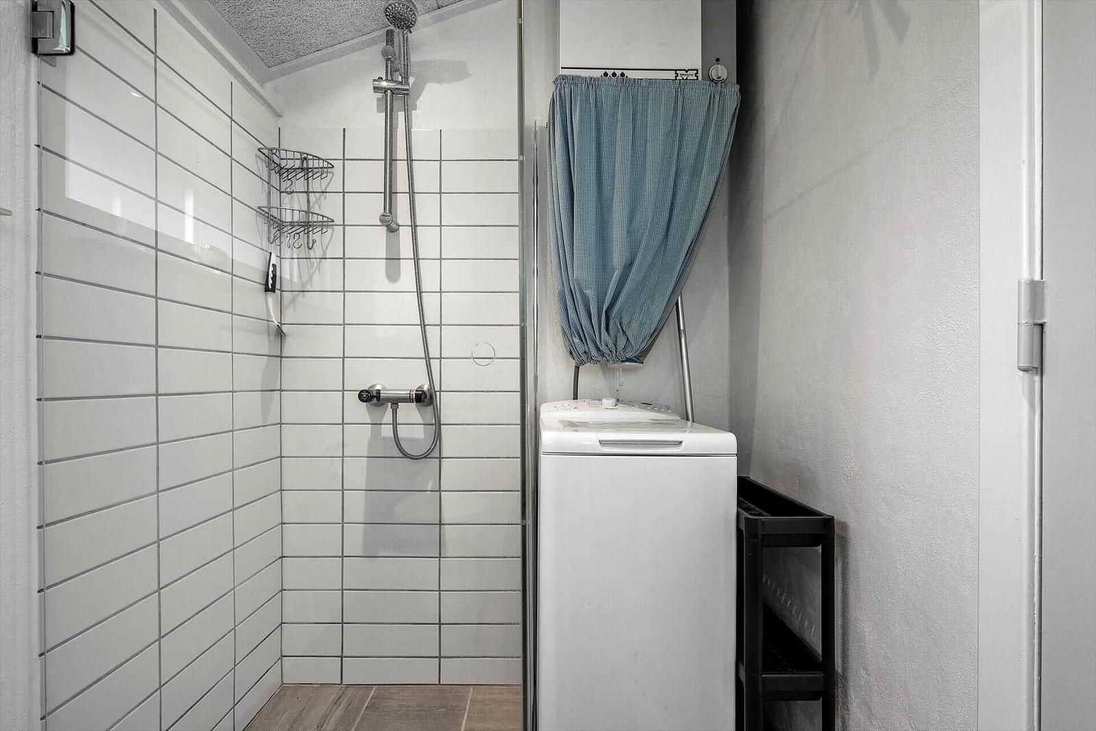 Dusche mit Duschbrause und Waschmaschine im Bad.