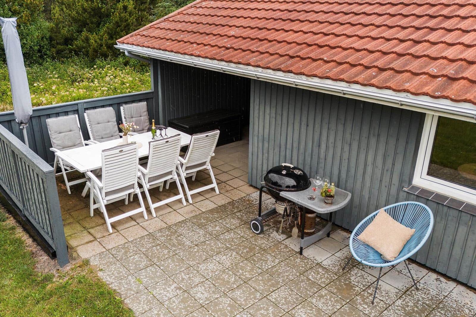 Terrasse mit Tisch, Stühlen, Grill und blauem Sessel.