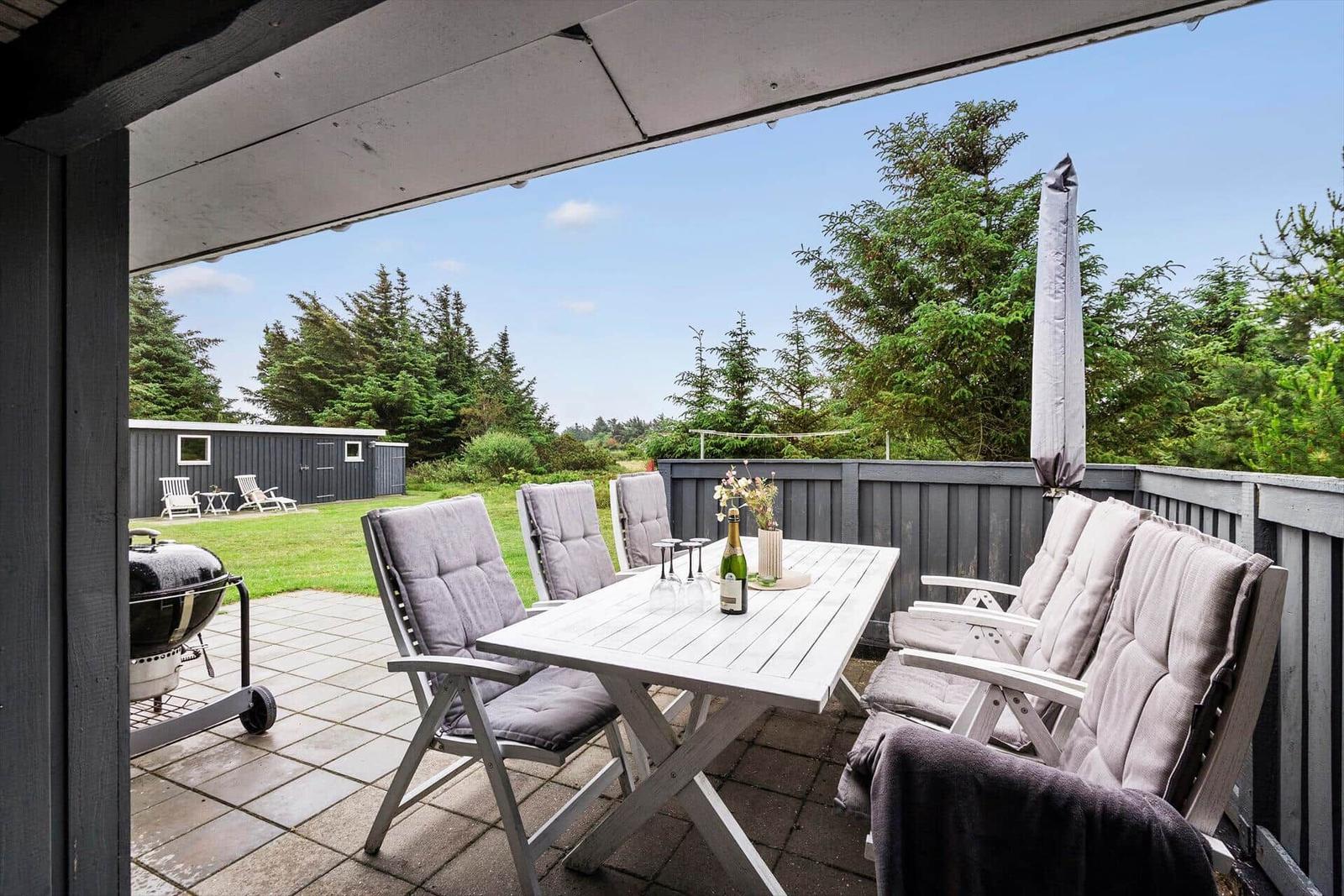 Terrasse mit Tisch, Stühlen und Grill. Hinterhof mit Grünfläche und Bäumen.