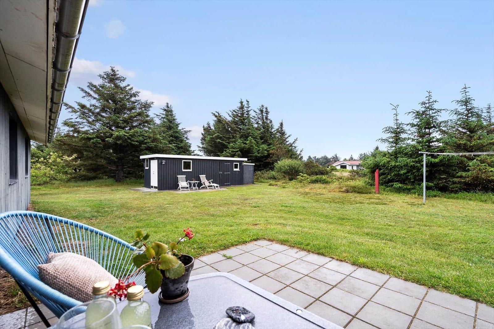 Terrasse mit blauem Stuhl und Tisch. Grünfläche, kleiner Gartenhaus im Hintergrund.