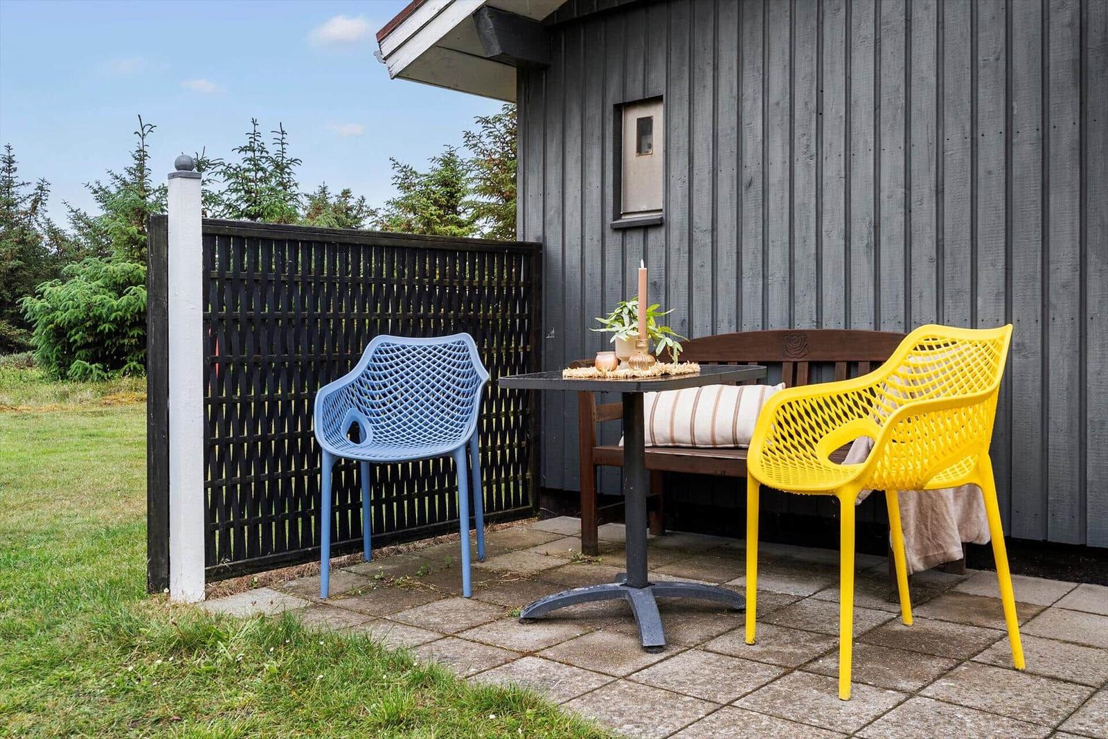 Terrasse mit Tisch, gelber und blauer Stuhl, Holzbank und Pflanzen.
