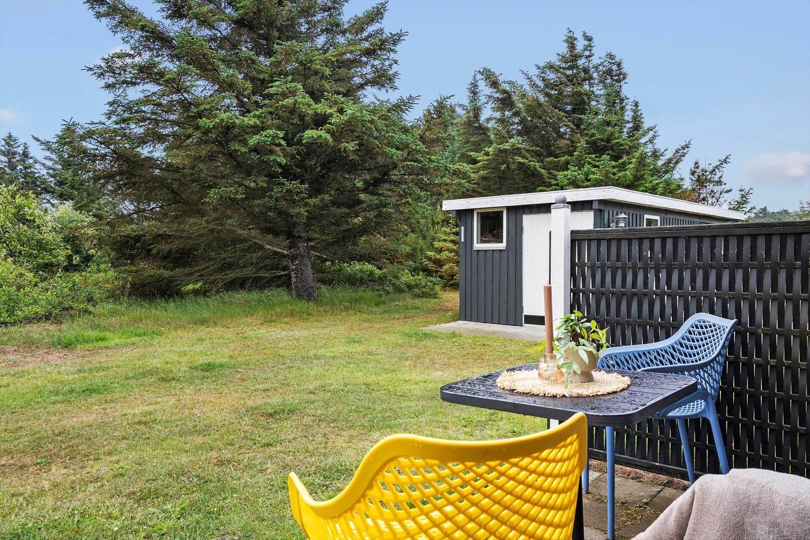 Außenbereich mit Tisch, gelber und blauer Stuhl, Grasfläche und kleinem Haus.