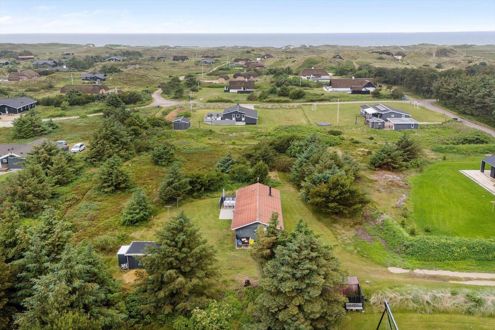 Haus mit rotem Dach und Garten, umgeben von Grünflächen und Bäumen. Blick auf die Küste.