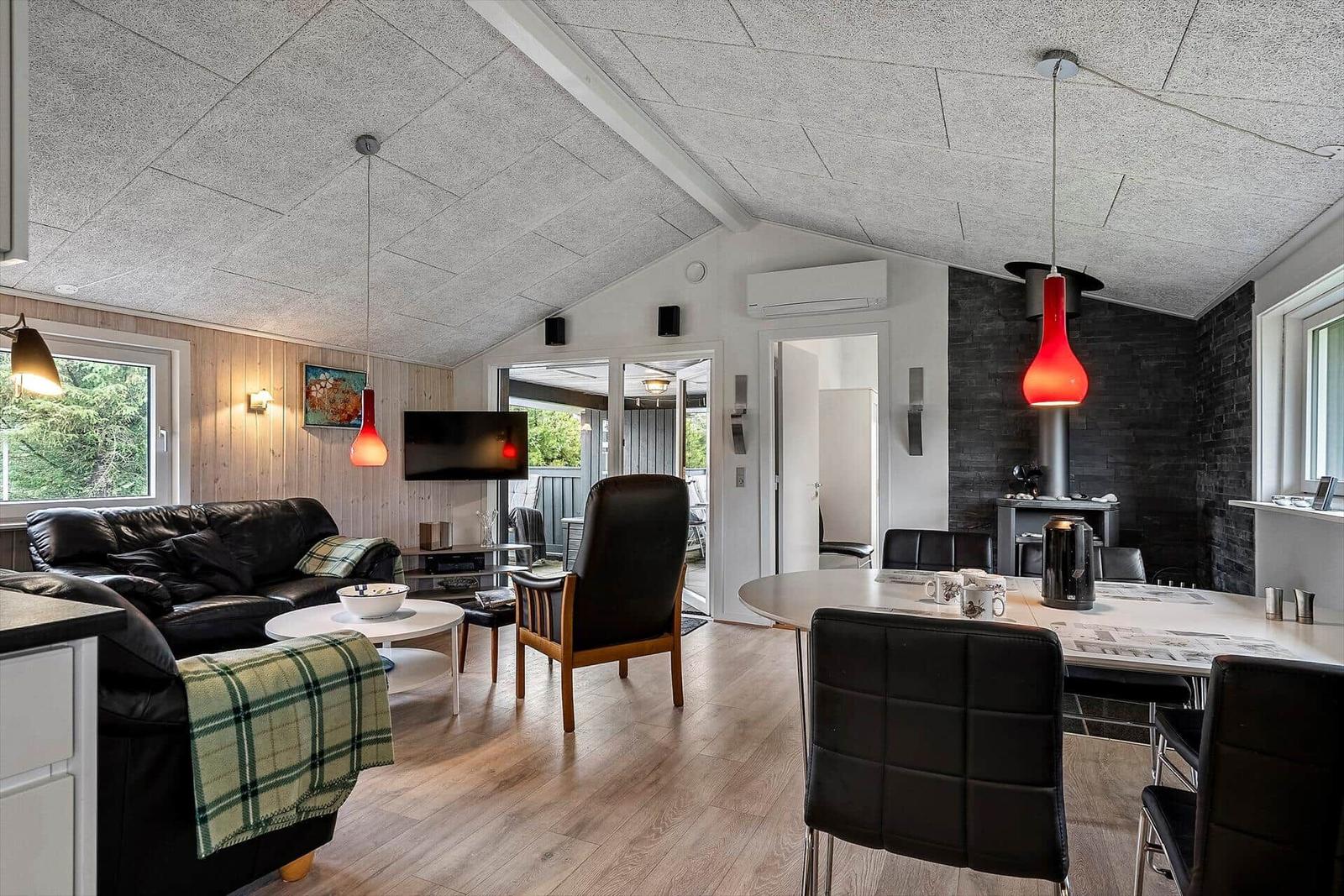 Wohn- und Essbereich mit Sofa, Tisch und Stühlen. Rote Lampen und Holzboden.