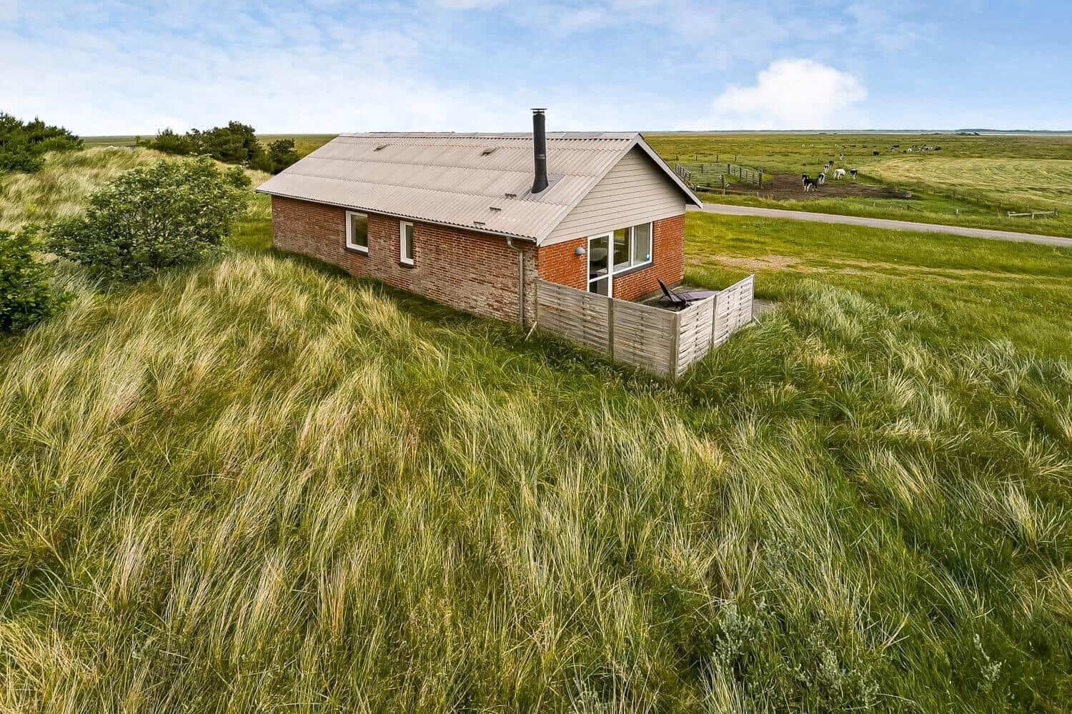Ein kleines Haus mit rotem Backstein und Holzveranda in einer grünen Wiese.