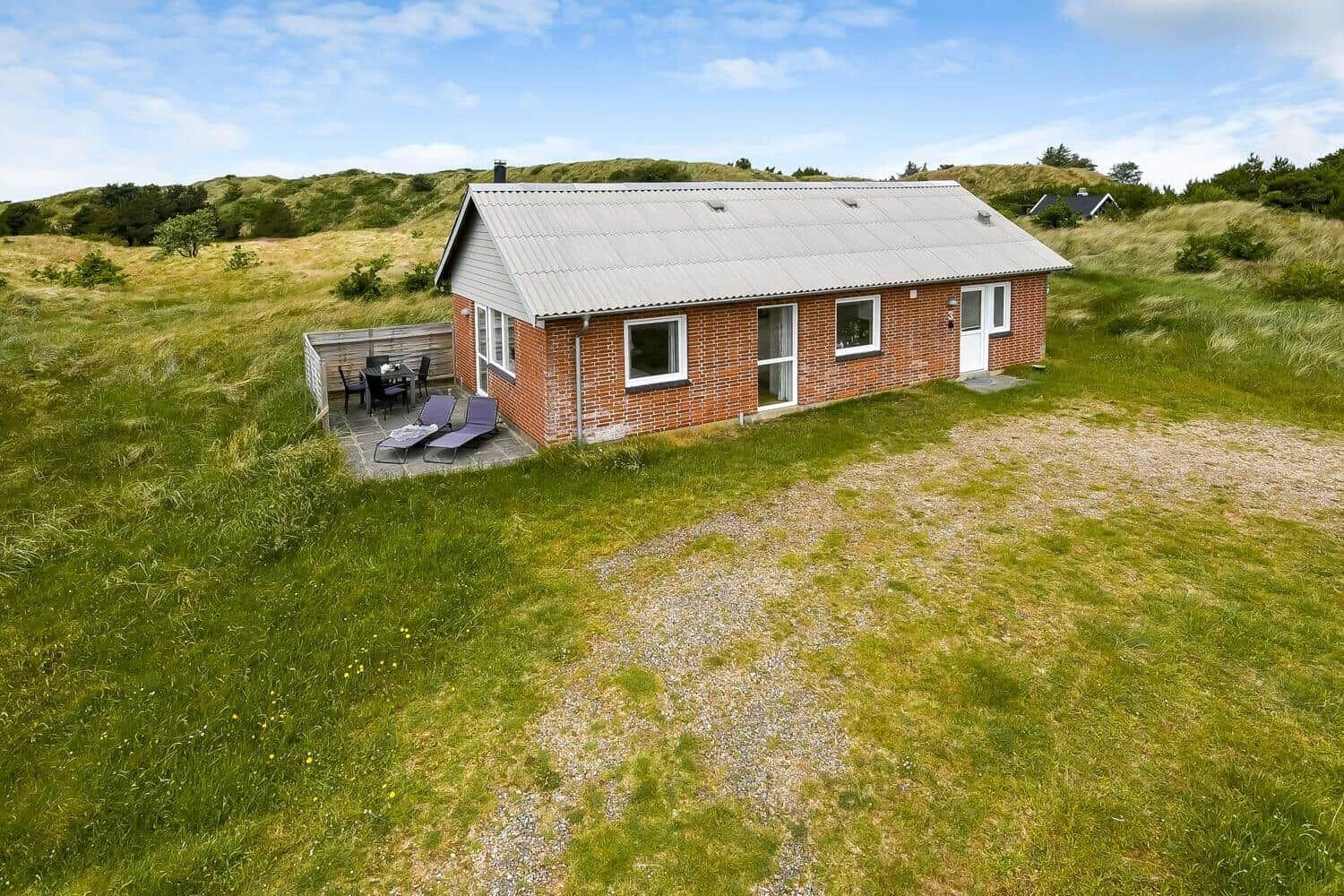 Ein kleines Haus mit Terrasse und Liegestühlen in einer grünen Landschaft.