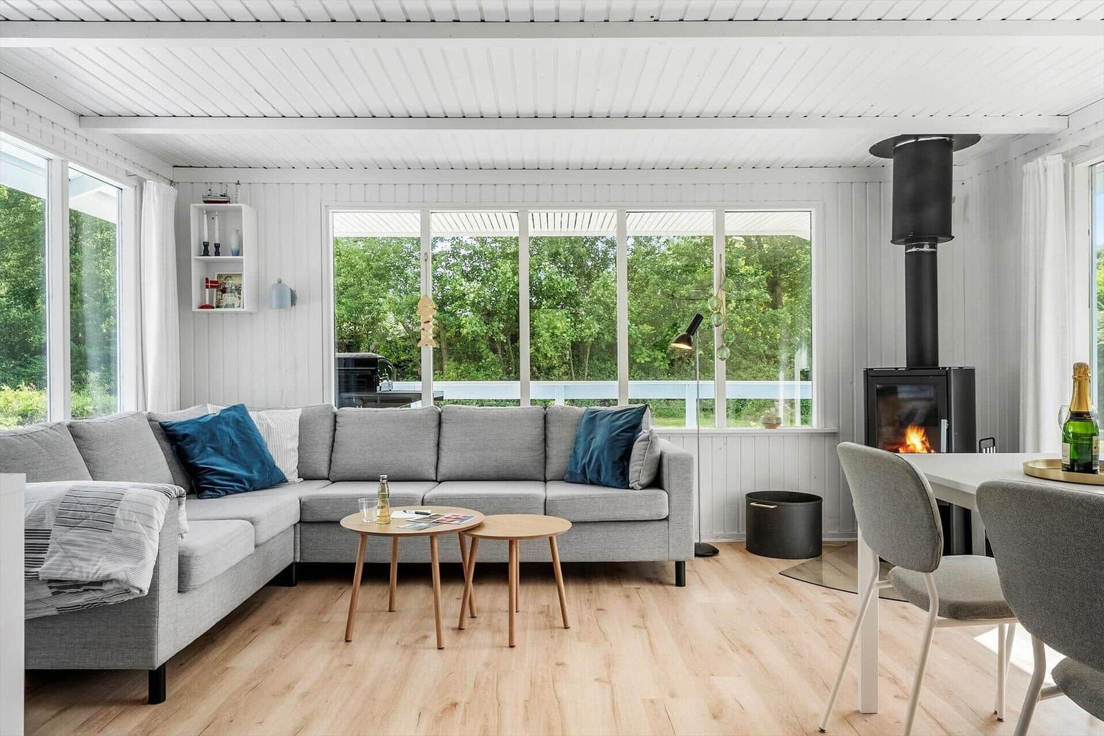 Wohnbereich mit Sofa, Tisch und Kamin. Große Fenster mit Blick auf Grün.